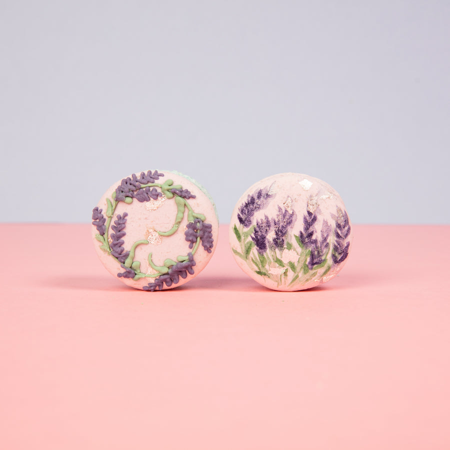 Lavender-themed artisan macarons with hand-painted floral design on pink surface
