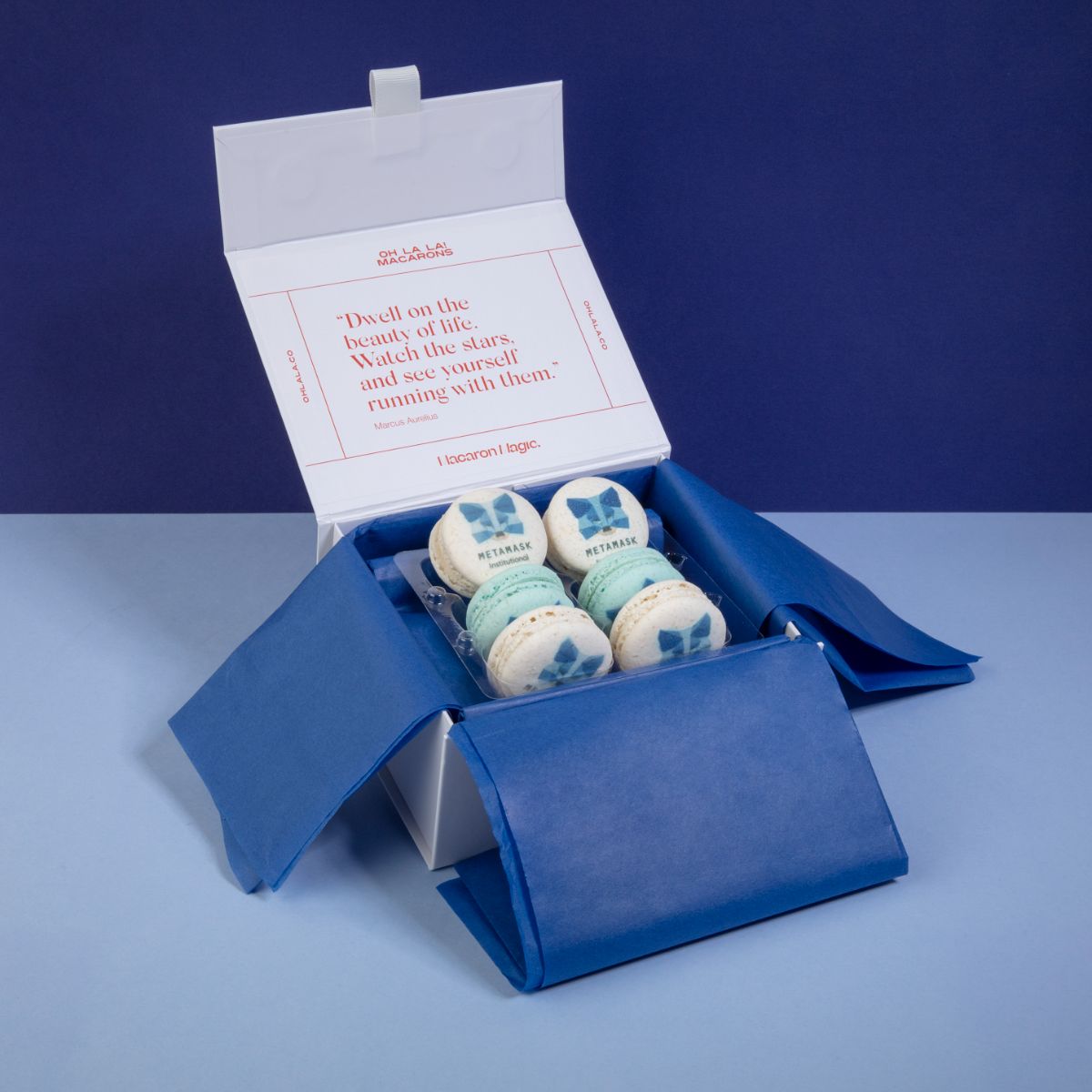 A small box lined with blue tissue paper containing bespoke white and blue macarons