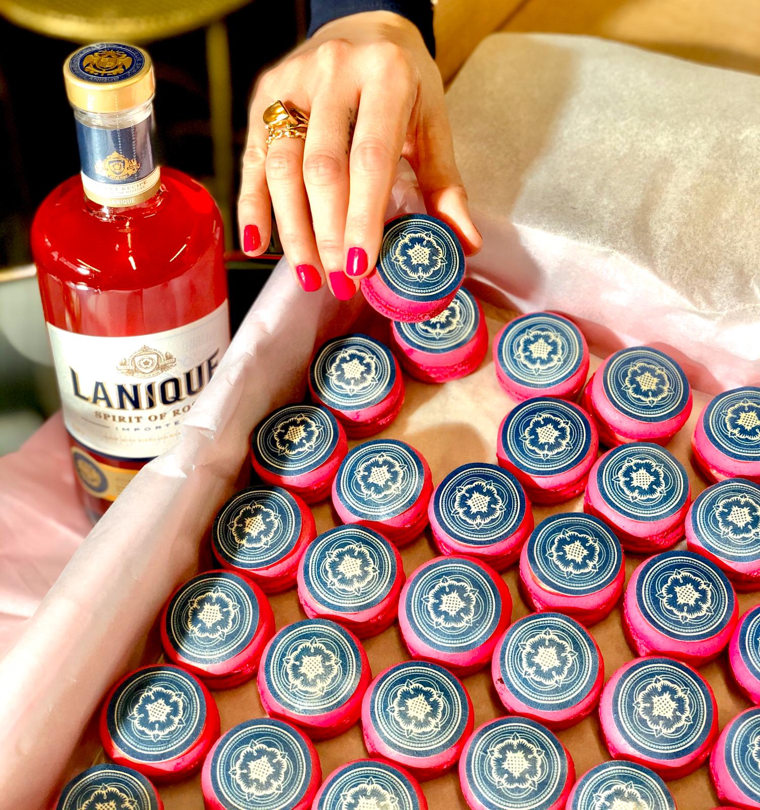 Woman's hand grabbing printed red macaron from a box next to a bottle of Lanique