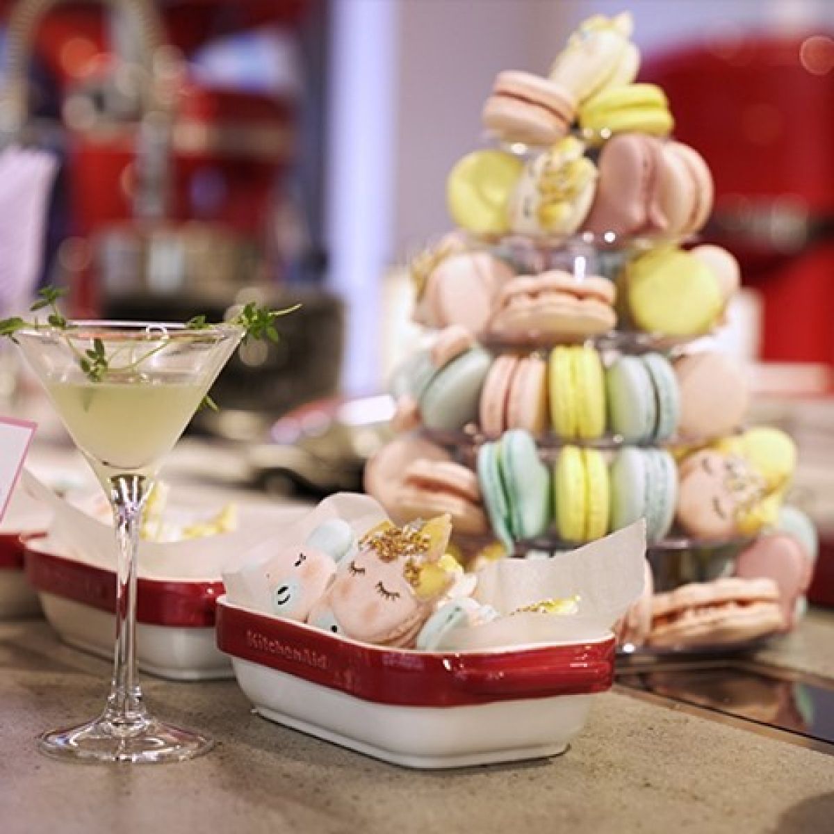 A yellow martini with garnish and an assembly of pink, blue, and yellow macarons at Oh La La! Macarons