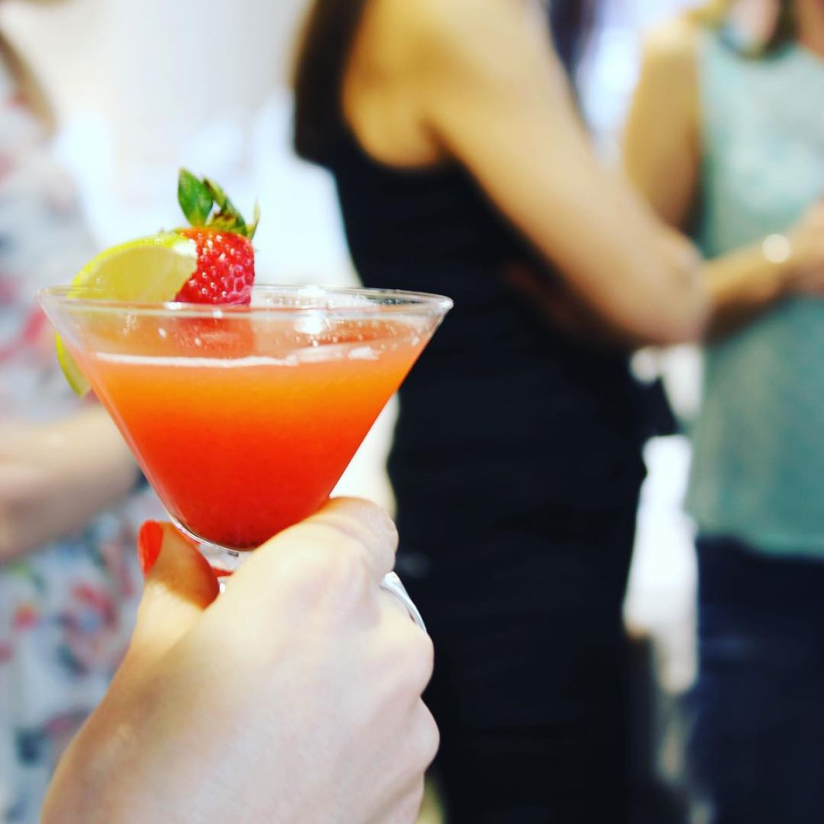 A woman's hand holding a martini topped with a strawberry and lemon at a hen party at Oh La La! Macarons