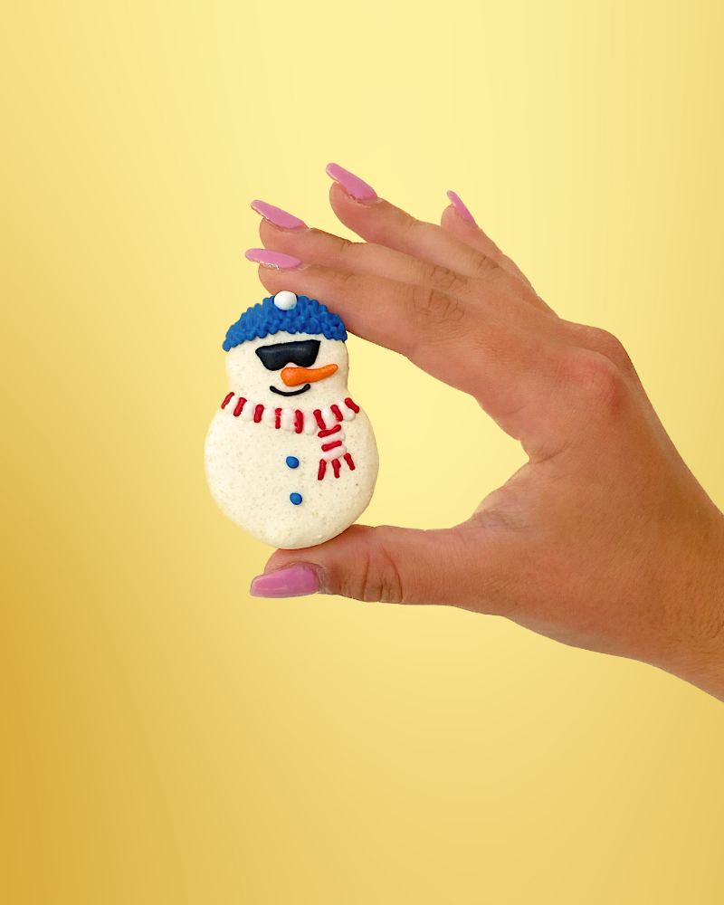 A hand holding a macaron decorated as a snowman with sunglasses at Oh La La! Macarons
